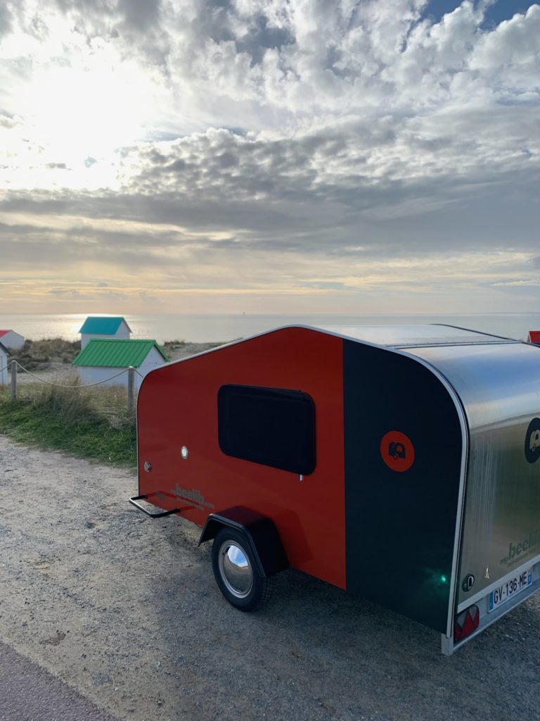 Caravane beelib rouge et grise en bord de mer pour les vacances