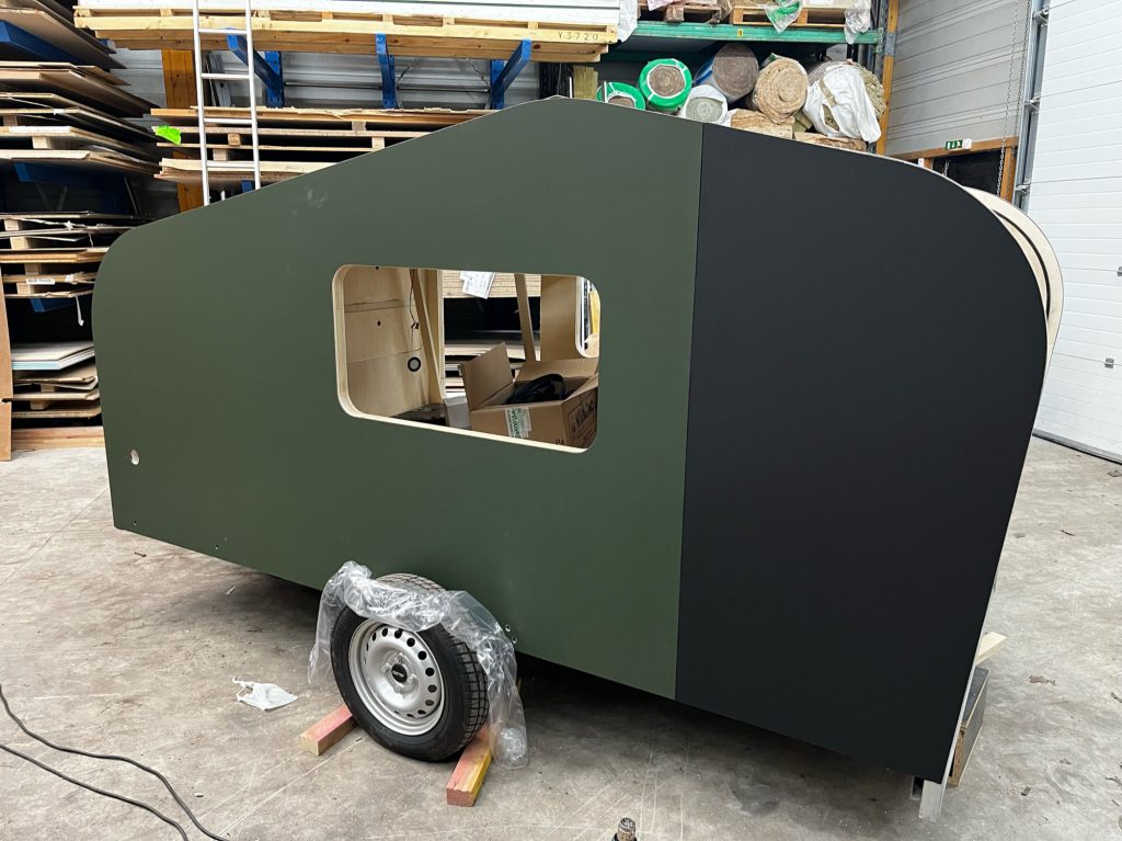 Teardrop caravane en atelier avec habillage vert mat et noir, fenêtre latérale découpée et roue montée, carrosserie en cours de finition.