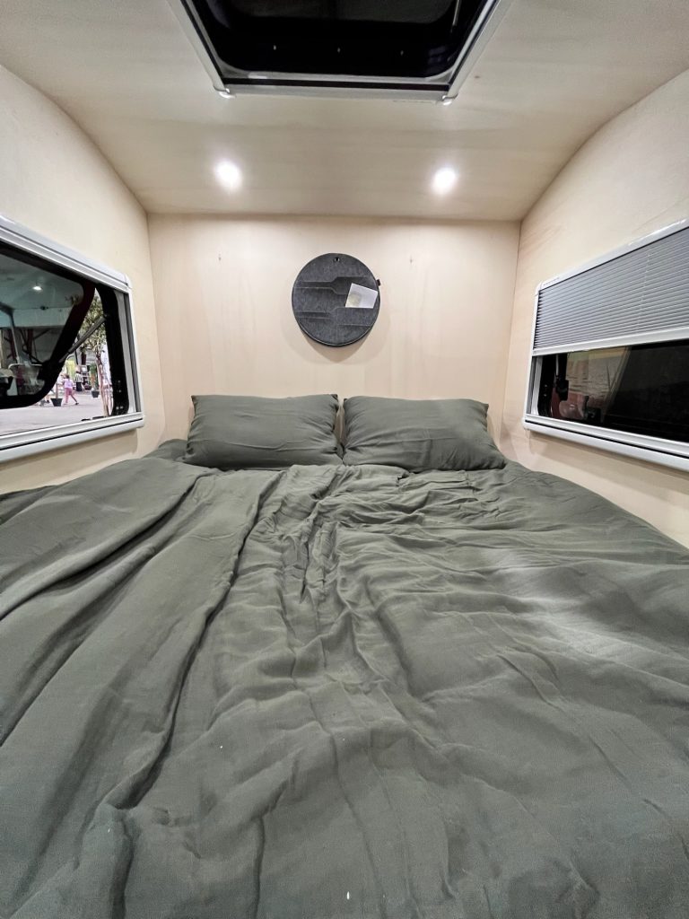 Tear Drop intérieur : lit double avec éclairage LED et lanterneau au plafond, deux fenêtres avec stores de chaque côté.